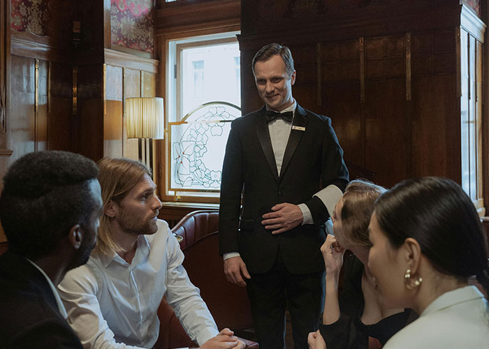 Waiter in a luxury setting serving a group, illustrating insights on what the rich pay for that are rip-offs in luxury industries.