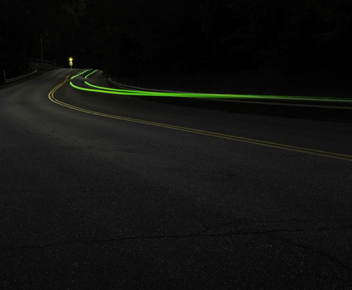 Dark empty road at night with green light trails curving along the street, capturing things people start to question seeing.