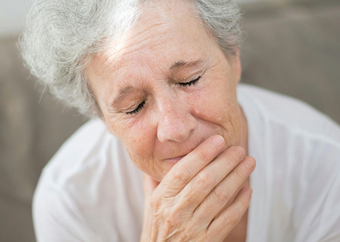 Elderly woman with gray hair crying and covering her mouth, experiencing shock from unhinged things her MIL said.