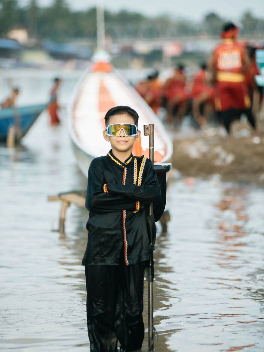 Young boy in traditional attire and futuristic sunglasses standing beside a boat in an unforgettable 2025 pop culture moment.