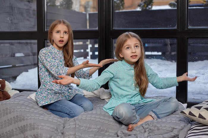 Two young girls sitting indoors by a window, expressing confusion and frustration highlighting big family drama moments.