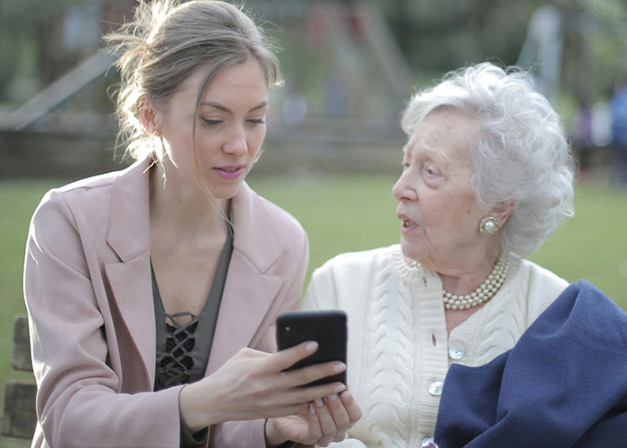 Young woman showing phone to elderly woman outside, capturing moments of unhinged things said by her MIL.