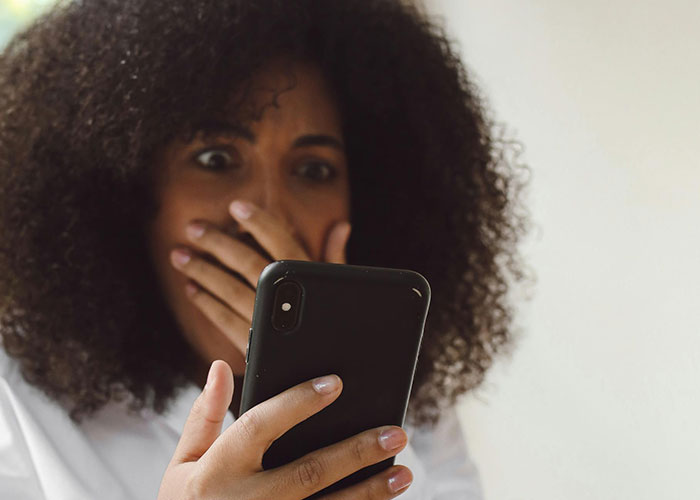 Woman with curly hair looking shocked while holding phone, reacting to insane ex stories shared online.