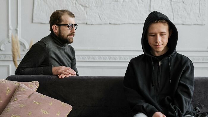 Man with glasses in black turtleneck talking to teenage boy in black hoodie, highlighting ambiguous fault and right situations.