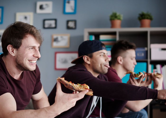 Three young men eating pizza and hanging out at home during a boys&rsquo; night, enjoying casual time together.