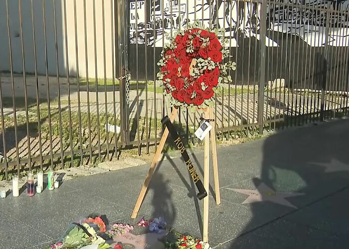 Memorial wreath and flowers near a star on the sidewalk honoring Father Rob amid reports on Nick Reiner's hotel room state.
