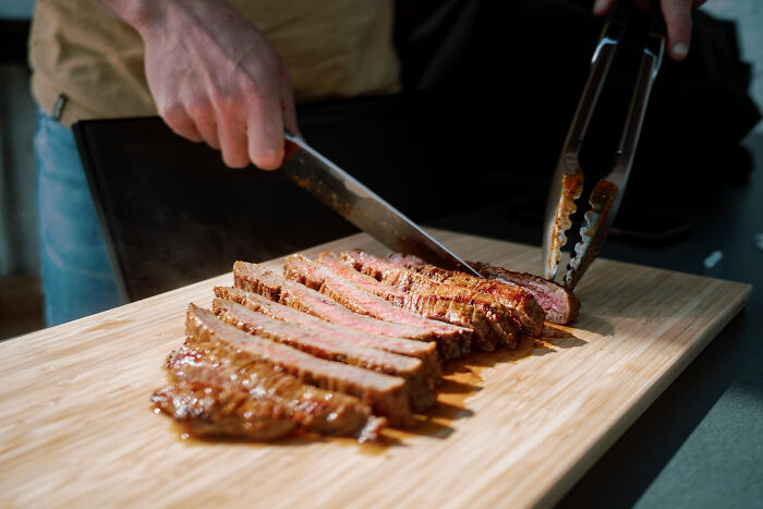 Person slicing grilled steak on a wooden board revealing dark dirty truths about the food industry hidden from employees.