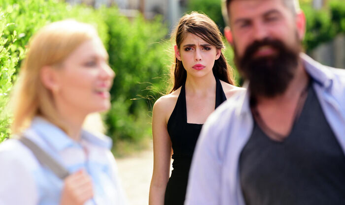Young woman looking upset and distant while a man and woman talk, showing signs of being stuck in high school era.