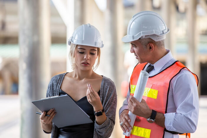 Two construction workers in hard hats discussing plans on site, illustrating infuriating work examples.