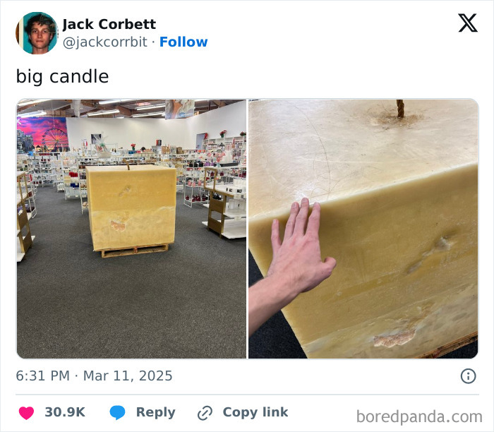 Giant yellow candle displayed in a store, with a hand showing scale against the candle’s large surface.