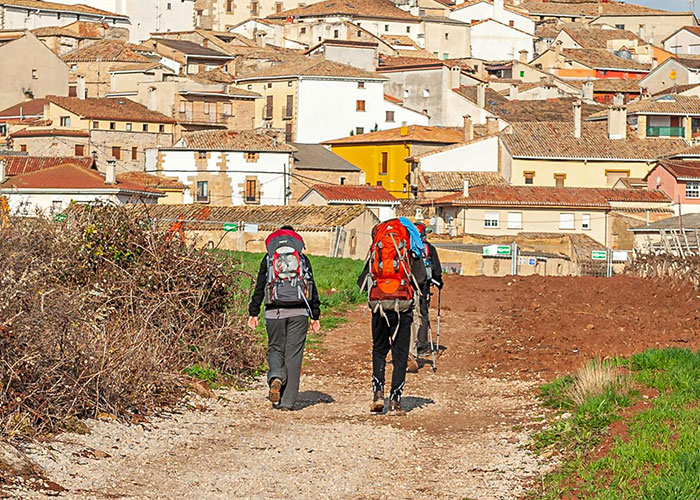Two hikers with backpacks walking on a path near a remote village, evoking creepy and mysterious isolated places.