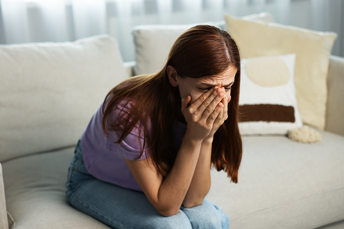 Woman sitting on couch with head in hands upset after family intervention over obsession with brother.
