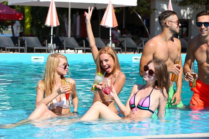 Group of friends enjoying drinks and laughing in a pool, capturing embarrassing moments people were blessed to see.