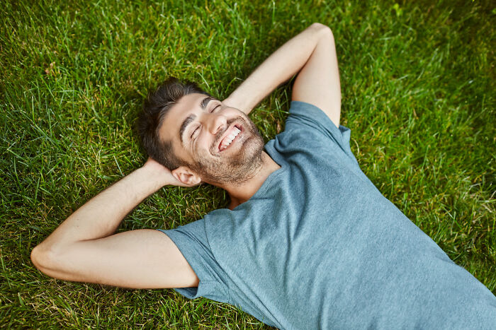 Man smiling with eyes closed, lying on grass, capturing an embarrassing moment people were blessed to see.