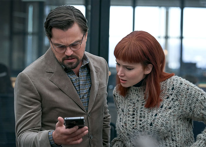 Jennifer Lawrence and Leonardo DiCaprio in an intense discussion during an indoor scene, focusing on a smartphone.