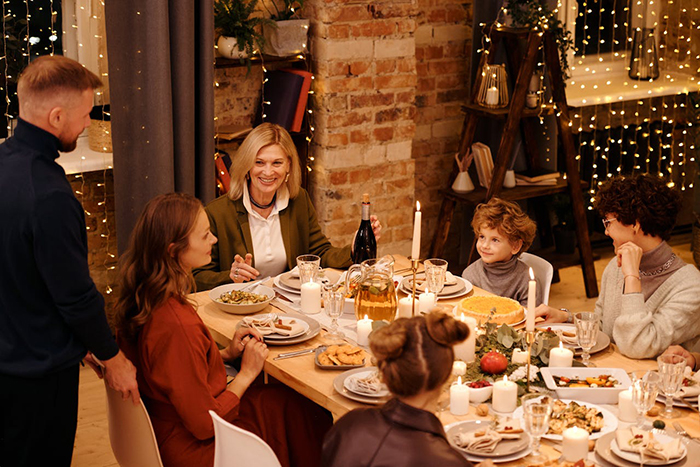 Family gathered around a festive dinner table, with step-grandma watching the baby during babysitting time near holiday lights.