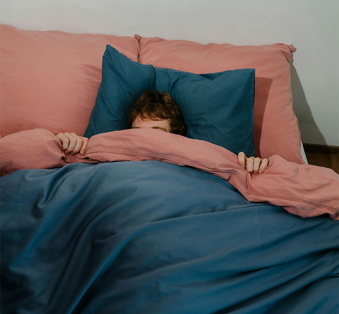 Person hiding under blue and pink bedcovers, illustrating themes of relationship lies and fear of losing partner.