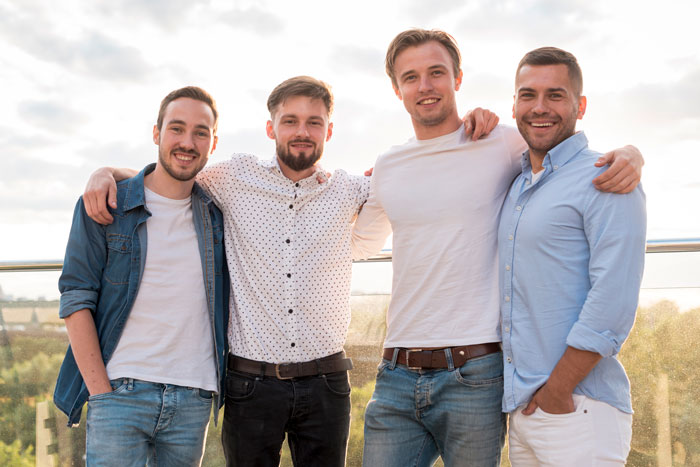 Four young men smiling and posing together outdoors, illustrating women ruining MIL’s surprise by pretending ignorance. Four young men smiling and posing together outdoors, illustrating women ruining MIL’s surprise by pretending ignorance.