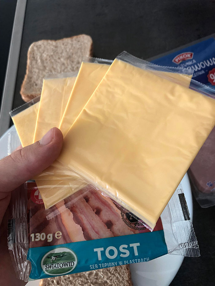 Hand holding multiple slices of processed cheese with sandwich bread in the background for McDonald&rsquo;s drive thru story.