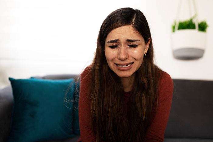 Young woman in a red top crying on a couch, illustrating emotional pain from marriage falling apart after wedding troubles.