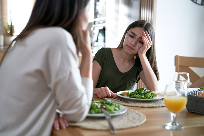 Woman loses appetite after seeing how mother-in-law prepares chicken, sitting at a dining table with salad plates and juice.