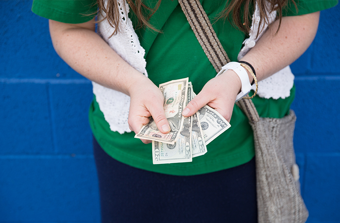 Teen holding cash in hands, standing against a blue wall, illustrating concerns about missing $30k and vague mom answers.