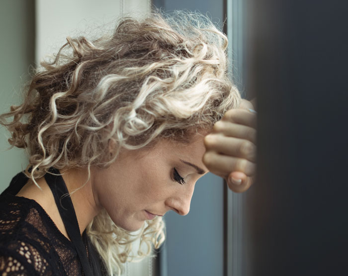 Woman with curly blonde hair leaning against a window, reflecting on forgiveness in challenging couples relationships.