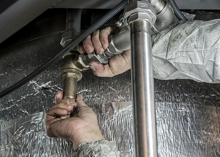 Hands of a worker adjusting pipes under a sink, illustrating luxury industries and costly rip-offs in plumbing services.