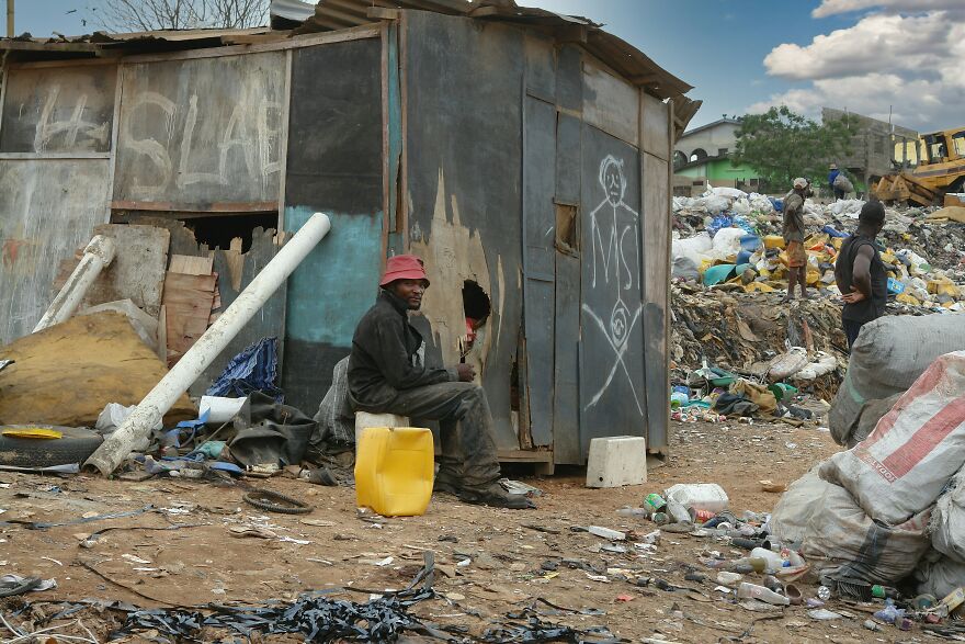 Man sitting outside a rundown structure surrounded by trash and debris in one of the dirtiest countries by pollution rankings