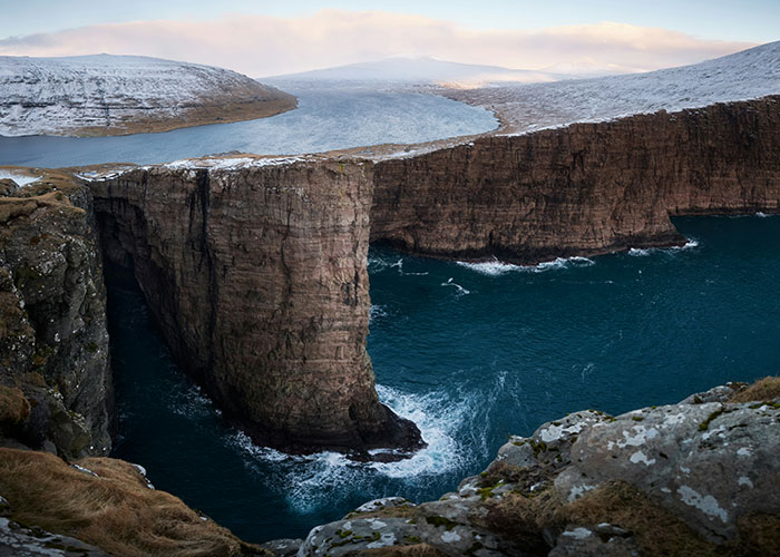 Steep cliffs rising from deep blue ocean with snow-dusted landscapes showcasing a place that looks AI generated but is real.