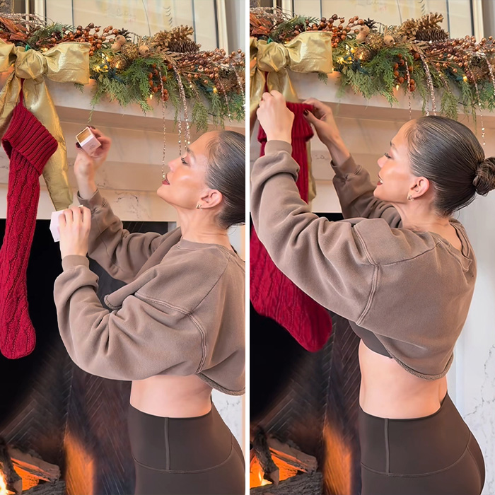 Jennifer Lopez hanging a Christmas stocking by a decorated fireplace in a festive holiday setting.