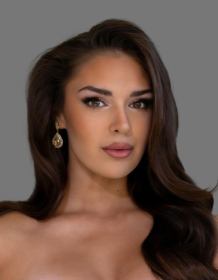 Miss Finland with long brown hair and earrings posing against a gray background in a beauty portrait.
