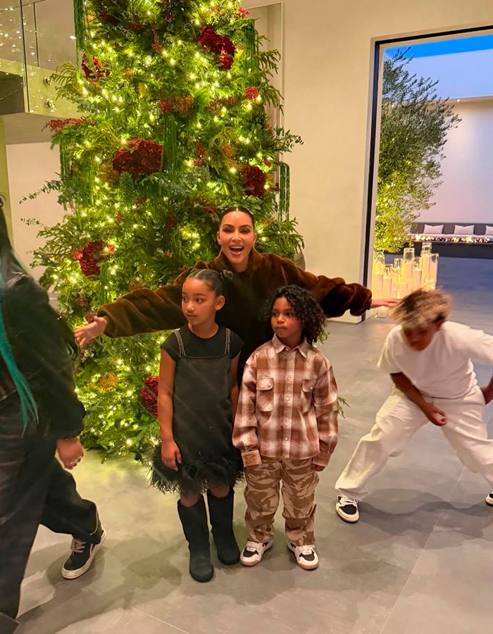 Kim Kardashian with her kids in front of a decorated Christmas tree, highlighting fans' views on kids' home life.