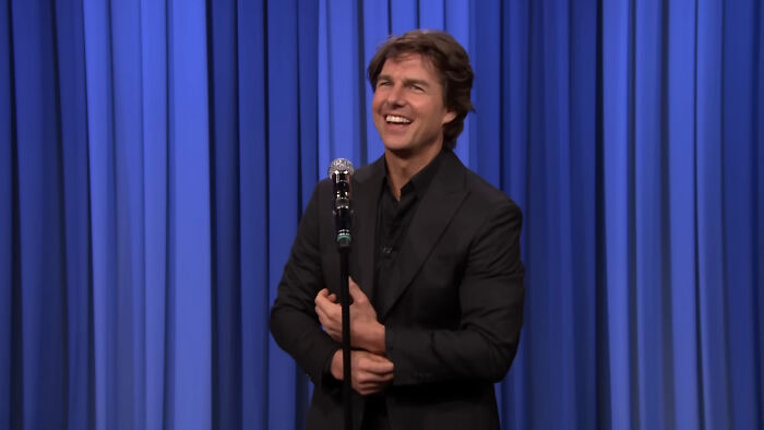 Man in black suit smiling on stage with microphone, illustrating people think celebrities closet skeletons theme.