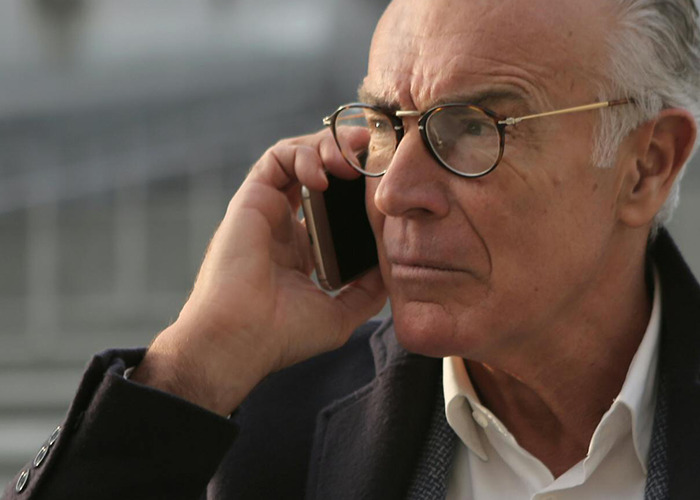 Elderly man with glasses holding a phone to his ear, portraying a 911 operator receiving non-emergency calls.