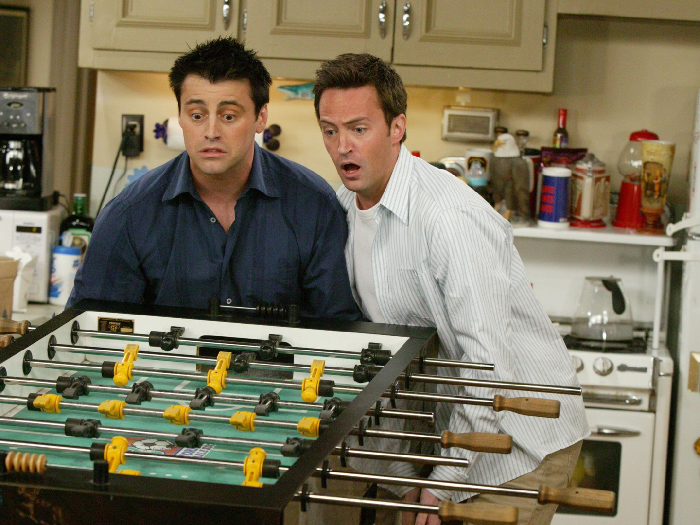 Two men in a kitchen focused on a foosball table, capturing fun moments in the city that never sleeps.