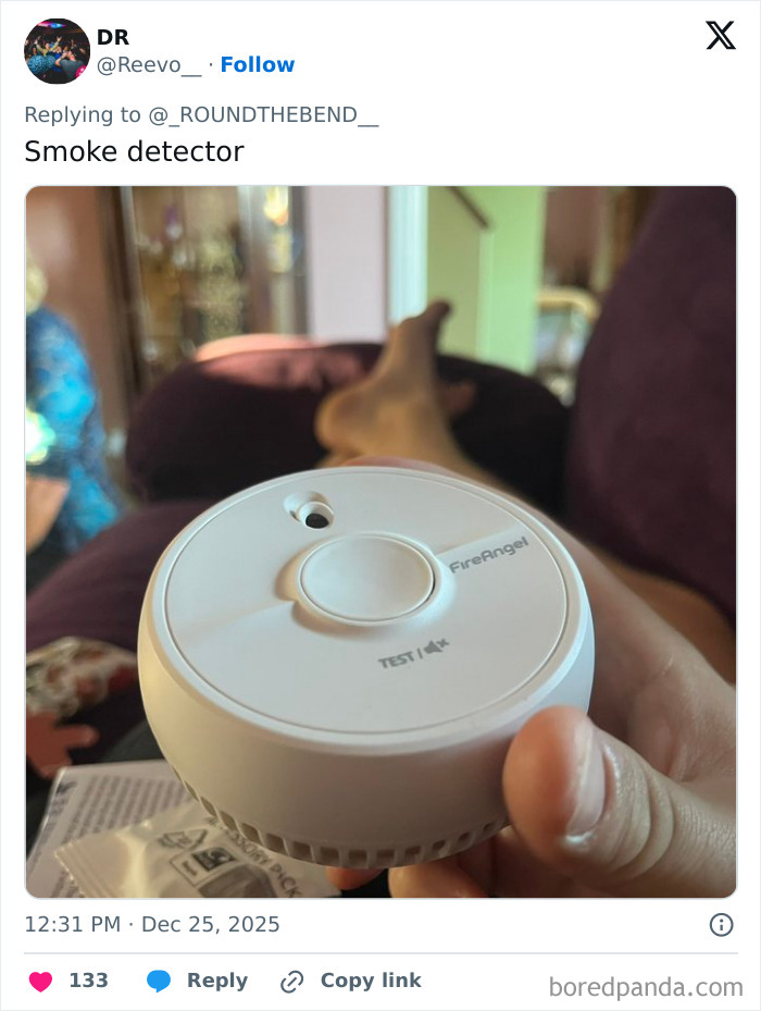 Hand holding a FireAngel smoke detector with blurred background, illustrating one of the worst Xmas presents received.