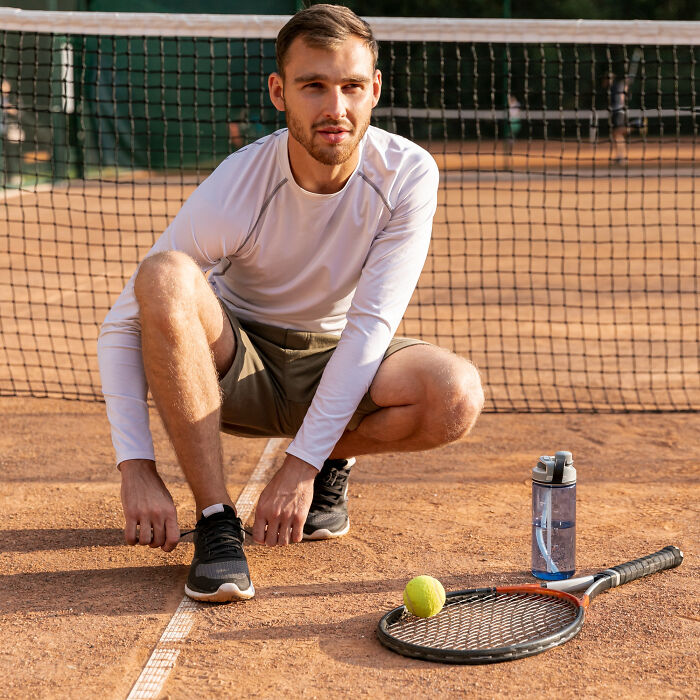 Young man squatting on tennis court near racket and ball, symbolizing men missed delivery babies concept.
