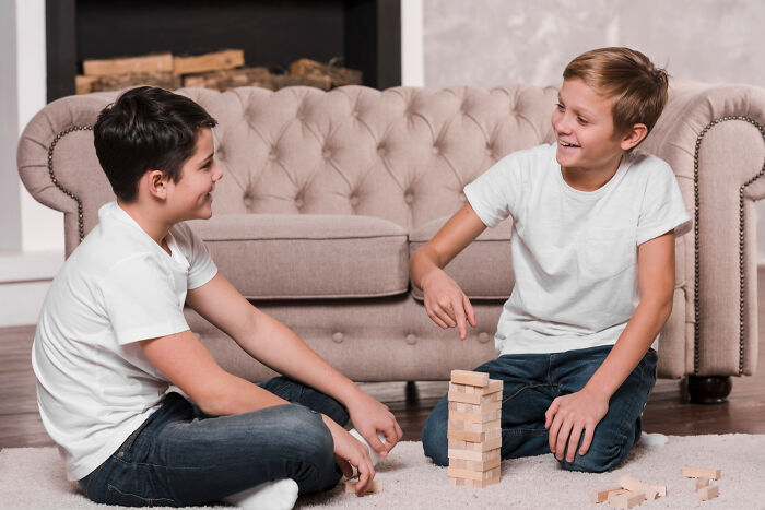 Two boys sitting on the floor playing a wooden block game, capturing a moment of strange and specific kid insults.