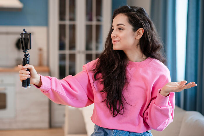 Young woman filming herself with a selfie stick at home, illustrating crazy things people do to make their ex pine for them.