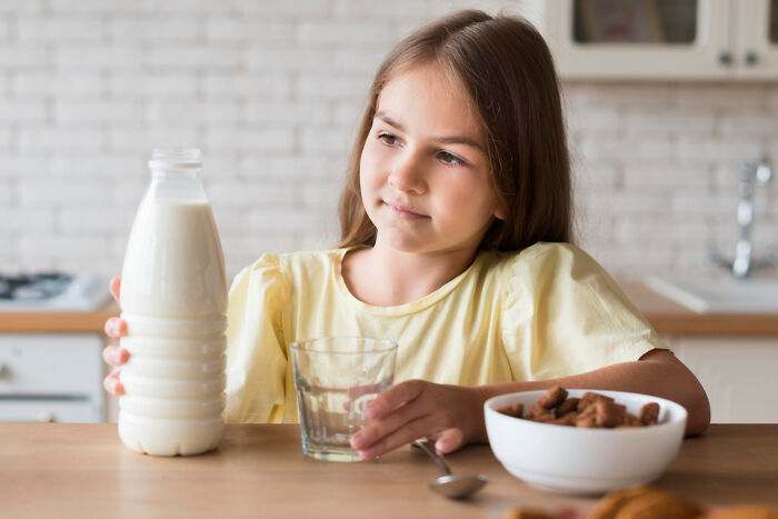 Young girl holding a bottle of milk and a glass in a kitchen, reflecting on a bitter revenge story experience.