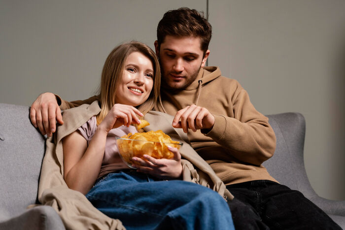 A young couple sharing a bowl of chips on a couch, capturing embarrassing moments people were blessed to see.