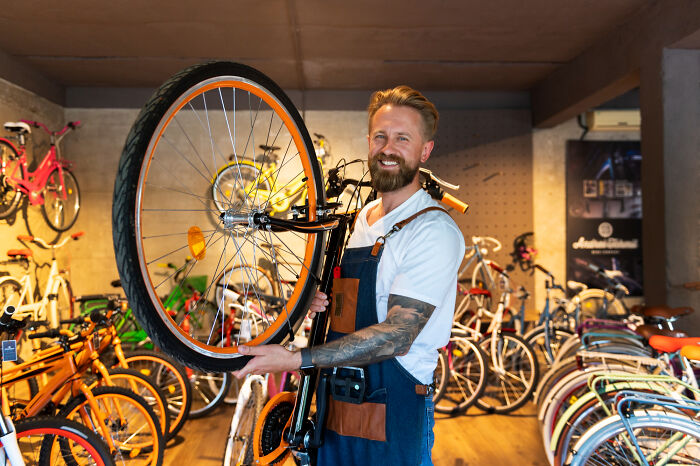 Man with tattoos holding a bicycle in a shop, representing a once-famous regular job in bike repair.