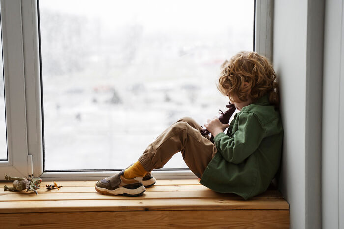Young child sitting by a window playing with toys, capturing a quiet moment amid family drama scenarios.