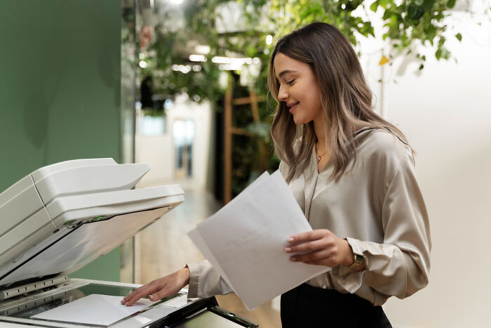 Woman using office copier with papers in hand, depicting common infuriating work examples of doing things the usual way