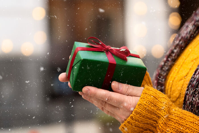 Person wearing yellow sweater holding a small wrapped gift box, illustrating small tricks for easier grown-up life.
