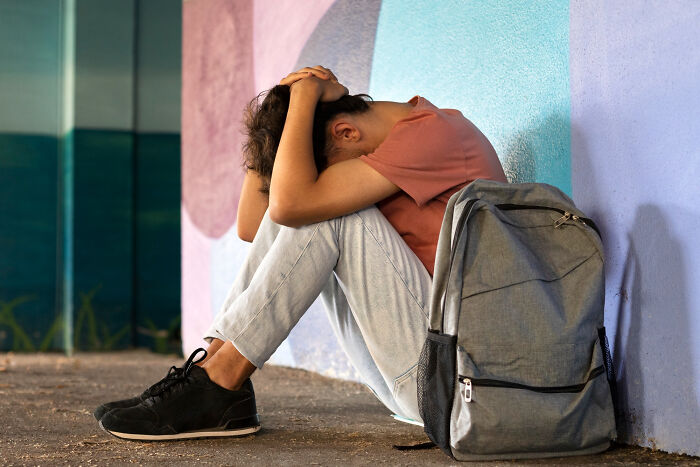 Teenage boy sitting against wall, head in hands, reflecting on revenge stories with bitter aftertaste and regret.
