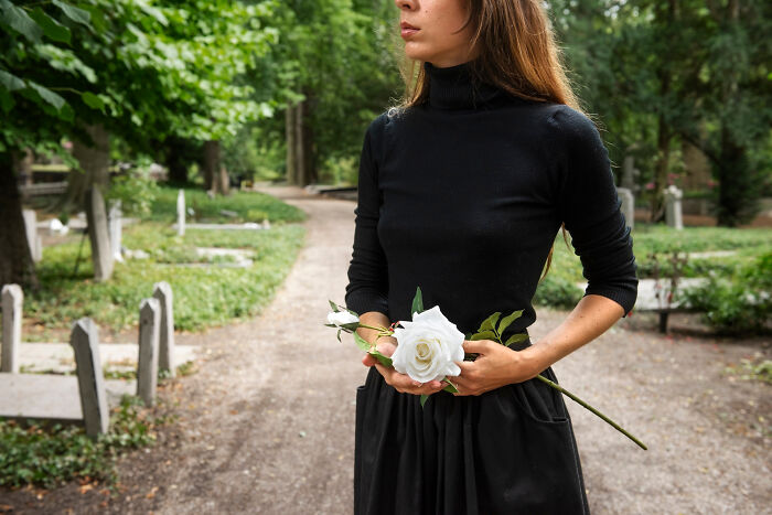 Woman in black dress holding white rose in a cemetery, capturing moments of unintentional big family drama emotions.