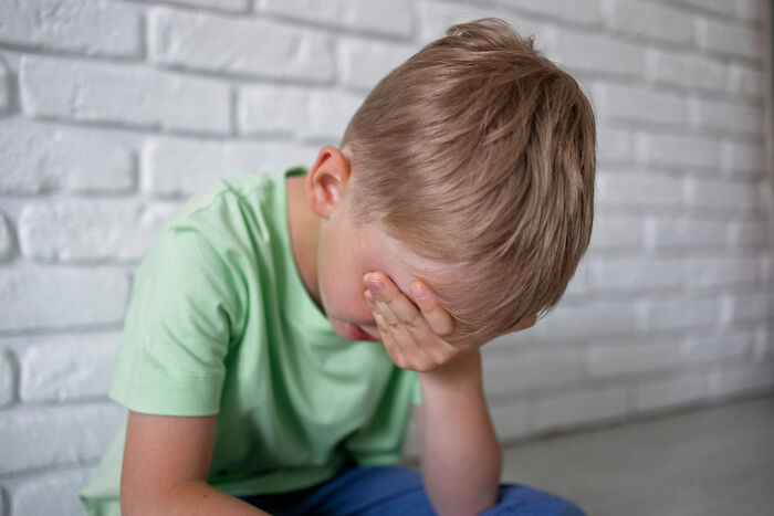 Young boy in green shirt covering his face, illustrating a kid's insult that is strange and specific.