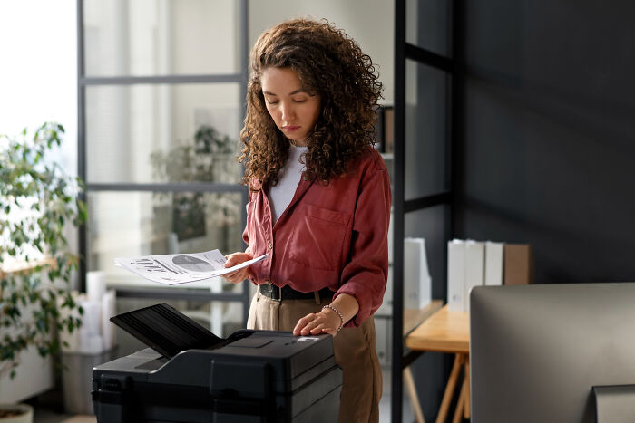 Woman in office using a printer, representing infuriating examples of we’ve always done it this way at work.